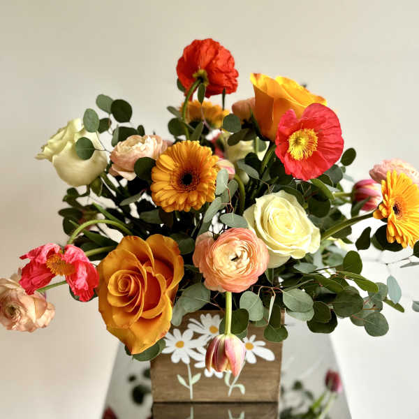 Mixed bouquet of orange, pink, red, and white flowers in a wooden box