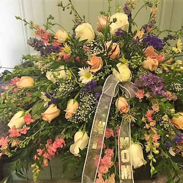 Large mixed floral spray with cream roses and purple accents, tied with a ribbon