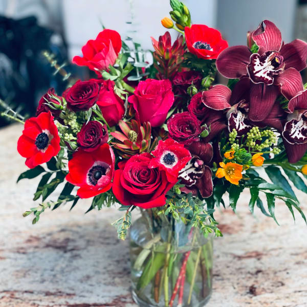 Bouquet of red roses and dark orchids in a glass vase
