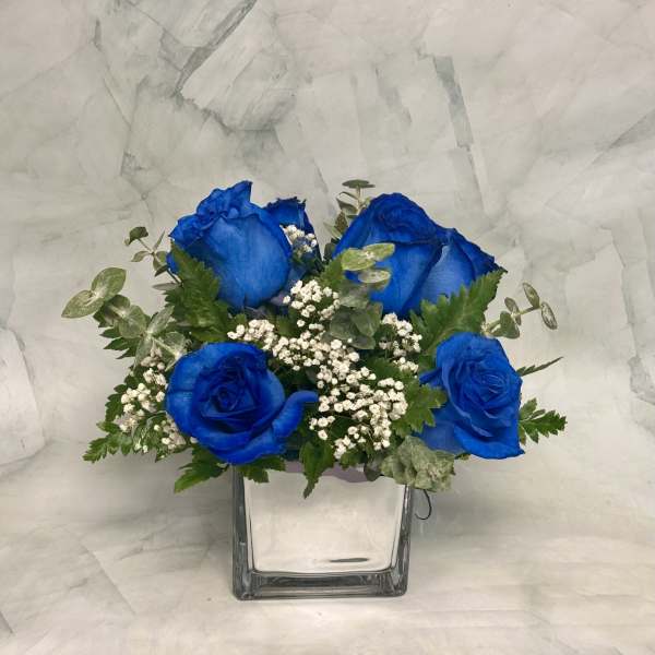 Blue roses in a clear square vase with baby's breath
