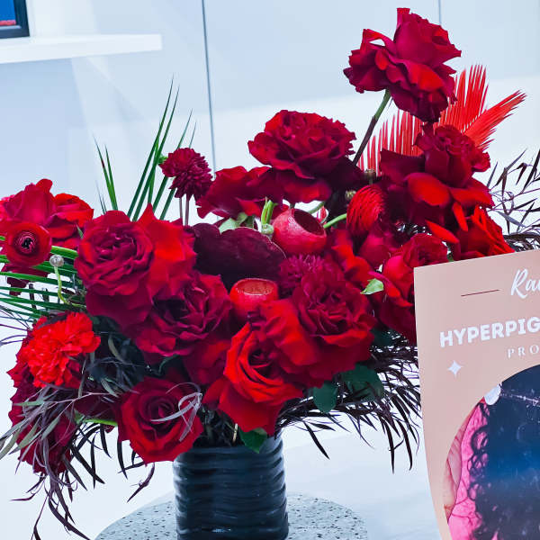 Red rose arrangement in a black vase with tropical foliage accents