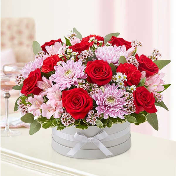 Red roses and pink chrysanthemums in a white hat box with a ribbon
