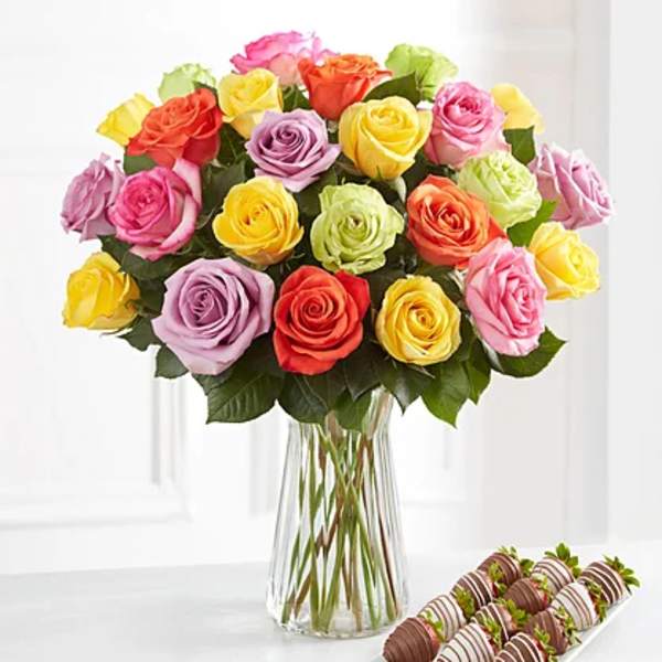 Colorful rose bouquet in a clear glass vase with chocolate-covered strawberries beside it