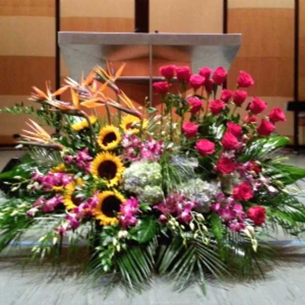 Large altar arrangement with pink roses, sunflowers, birds of paradise, orchids, and hydrangeas in a fan shape