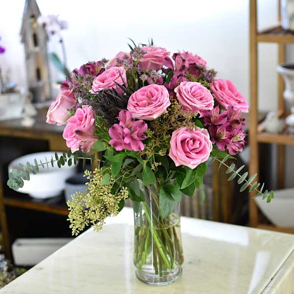 Pink roses and magenta flowers arranged in a clear glass vase