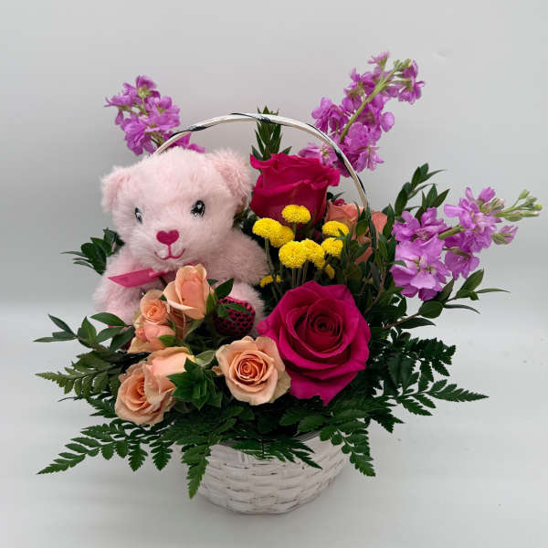 Pink teddy bear in a basket with roses and purple flowers