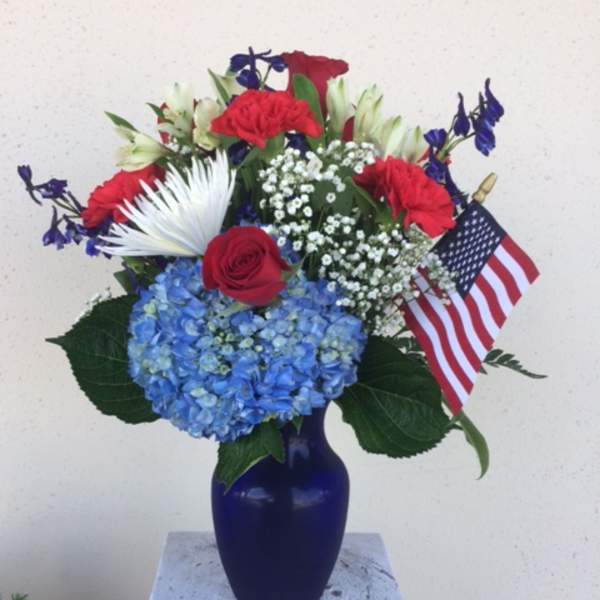 Red, white, and blue floral arrangement in a blue vase with an American flag