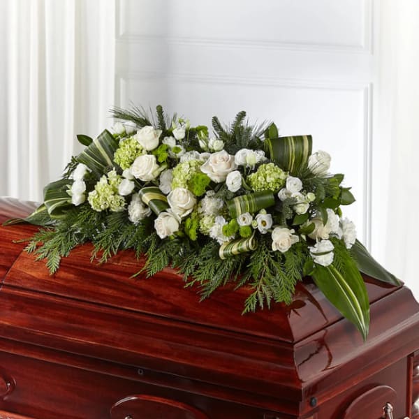 White and green floral casket spray on a polished wooden casket
