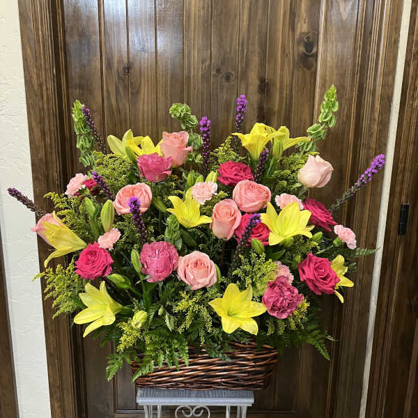 Basket arrangement of pink roses, yellow lilies, and purple spikes