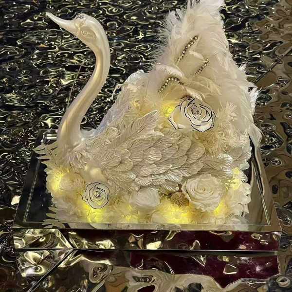White floral swan sculpture with feathers and roses on a mirrored base