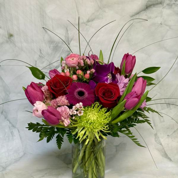 Mixed bouquet of pink, red, and purple flowers in a glass vase