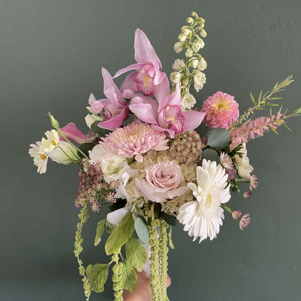Handheld bouquet of pink orchids, roses, and white daisies