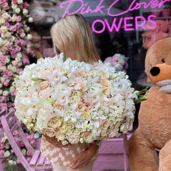 Large bouquet of white and blush flowers held in front of a flower shop