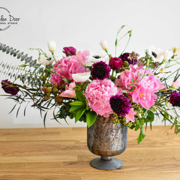 Low compote arrangement with pink peonies, white anemones, and dark purple blooms in a metal pedestal vase