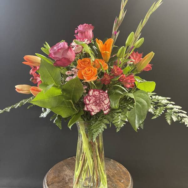 Mixed bouquet of orange and pink flowers in a clear glass vase