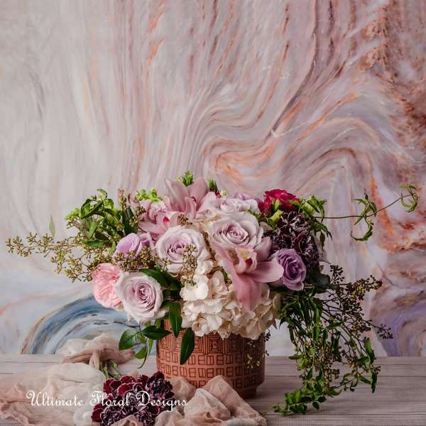 Pink and lavender roses with lilies in a patterned vase