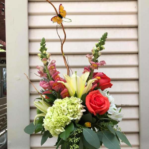 Mixed floral arrangement in a green vase with roses, lilies, and hydrangea