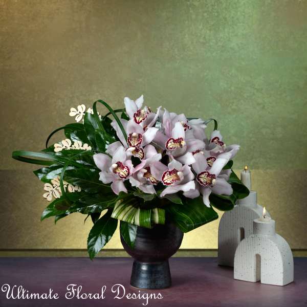 Pink orchids arranged in a dark vase beside lit candles