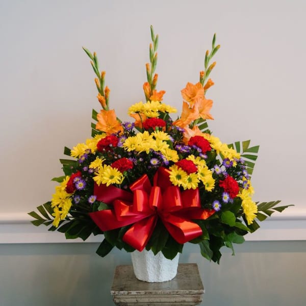 Colorful flower arrangement in a white vase with a red bow