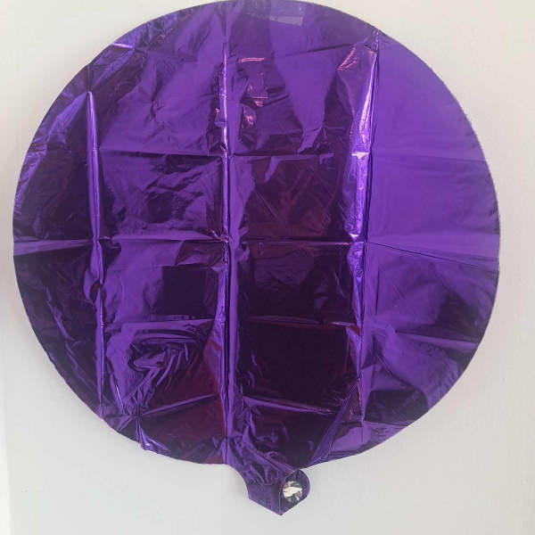Purple round foil balloon against a white wall