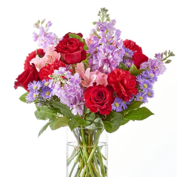 Bouquet of red roses, pink lilies, and purple flowers in a clear glass vase