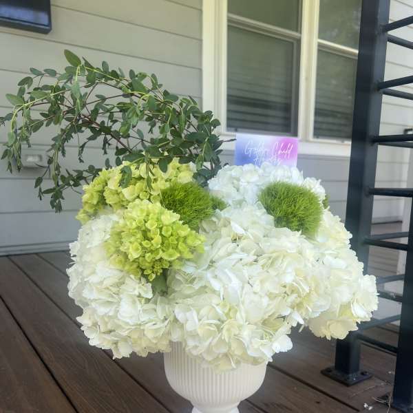 White and lime-green floral arrangement in a white pedestal vase