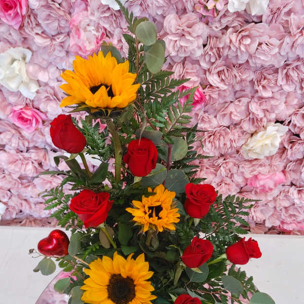 Red roses and sunflowers arranged in a tall vase with greenery