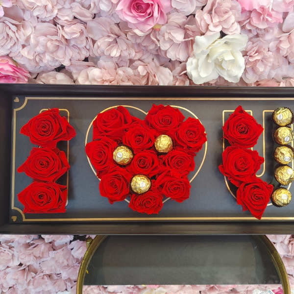Red roses and gold chocolates arranged in a framed display spelling love.