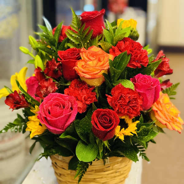 Basket arrangement of red, pink, orange, and yellow roses with carnations