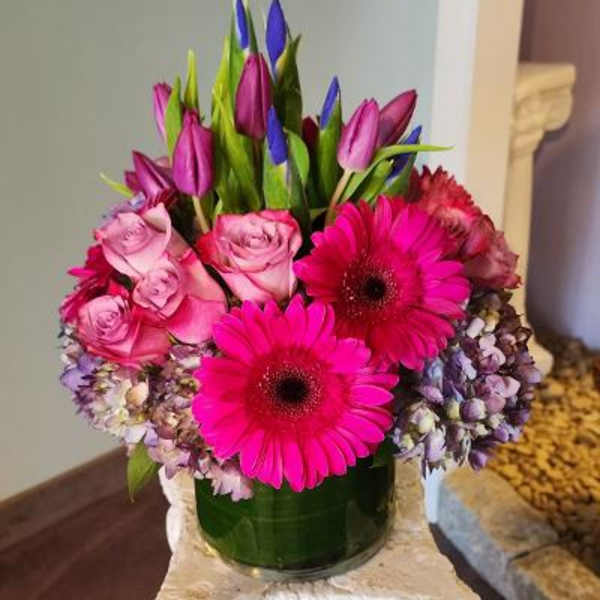Pink roses and gerbera daisies in a glass vase with purple tulips