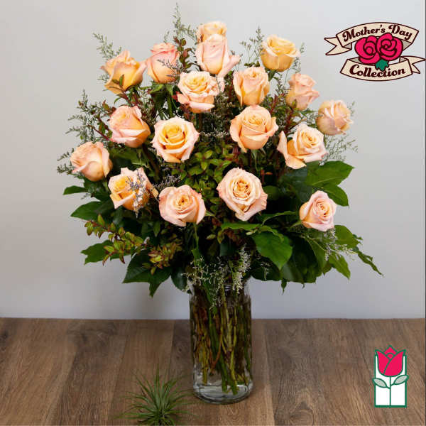 Peach roses arranged in a tall glass vase with greenery