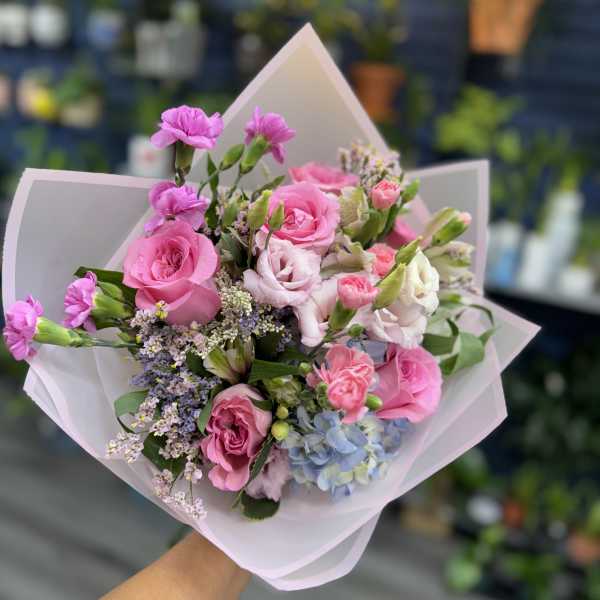 Pink rose bouquet with small purple and white flowers wrapped in pale paper
