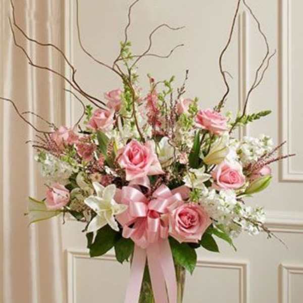 Tall pink and white arrangement with roses and lilies in a clear vase with a pink bow