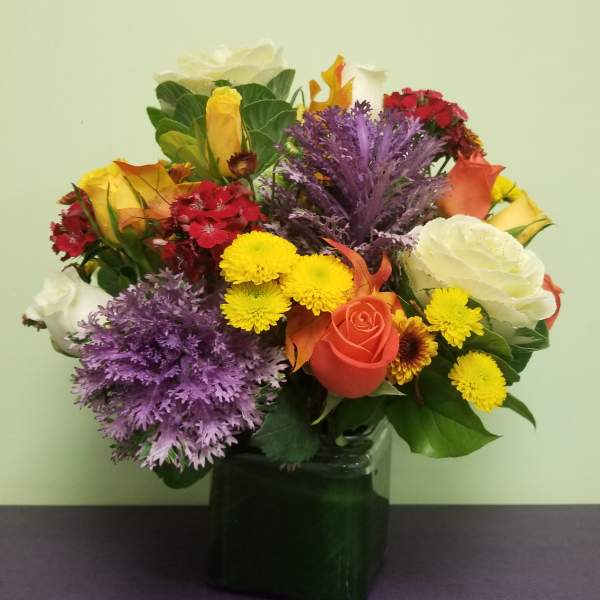 Mixed bouquet of roses, chrysanthemums, and carnations in a dark glass vase