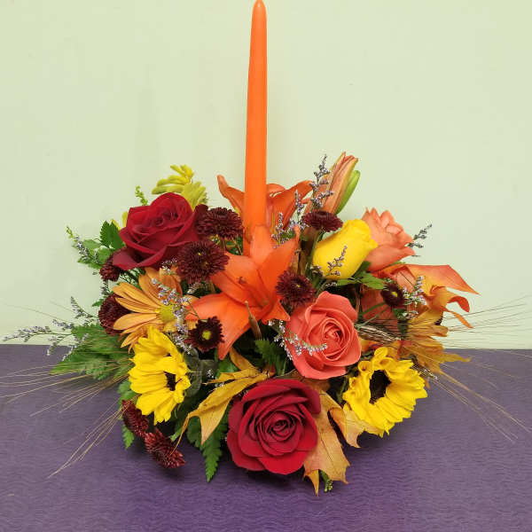Autumn floral centerpiece with roses, sunflowers, and a tall orange taper candle