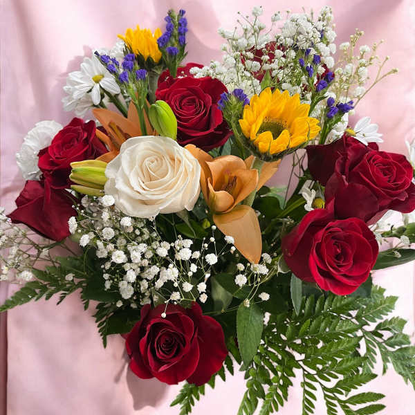 Bouquet of red and white roses with sunflowers and lilies on pink fabric