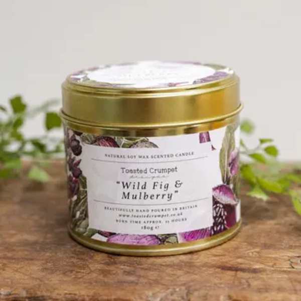 Gold tin candle labeled Wild Fig & Mulberry on a wooden surface