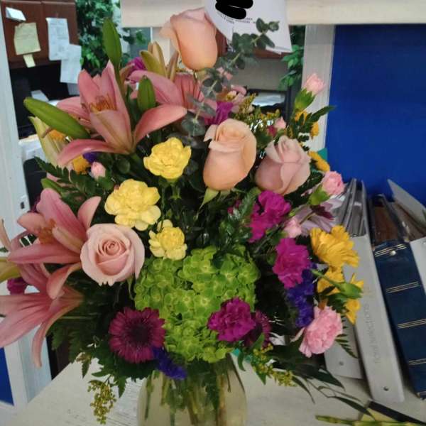Mixed bouquet of pink lilies, roses, hydrangea, and colorful filler flowers in a glass vase