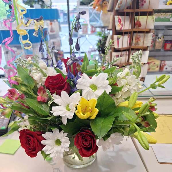 Mixed bouquet of red roses, white daisies, and yellow lilies in a glass vase