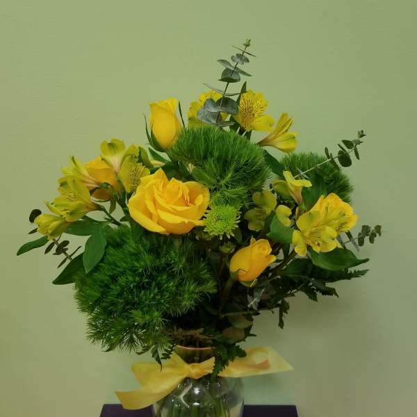 Yellow roses and alstroemeria in a glass vase with a yellow ribbon
