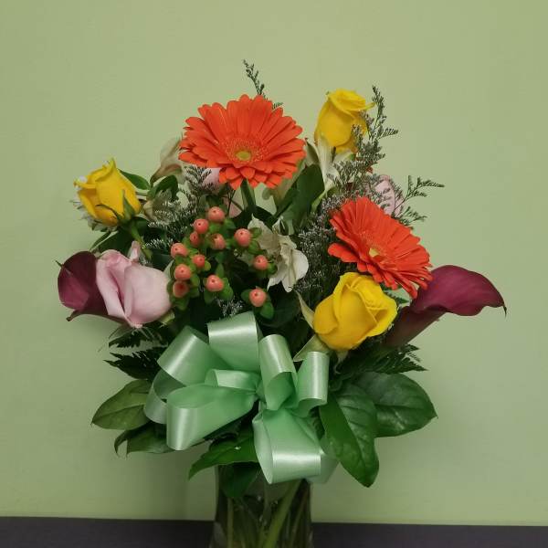 Bouquet of yellow roses, orange gerberas, and purple calla lilies in a glass vase
