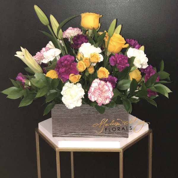 Mixed bouquet of yellow roses, lilies, and carnations in a rectangular box