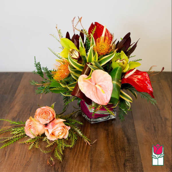 Tropical flower arrangement in a glass vase with a small rose cluster beside it