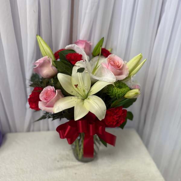 Bouquet of pink roses, white lilies, and red carnations in a glass vase