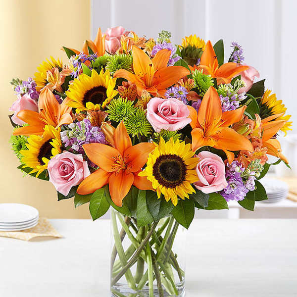 Bouquet of orange lilies, pink roses, and sunflowers in a glass vase