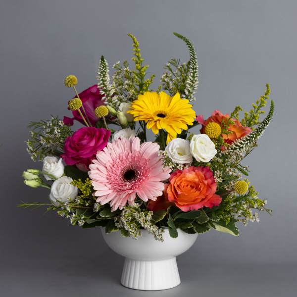 Colorful mix of gerbera daisies, roses, and lisianthus in a white pedestal bowl