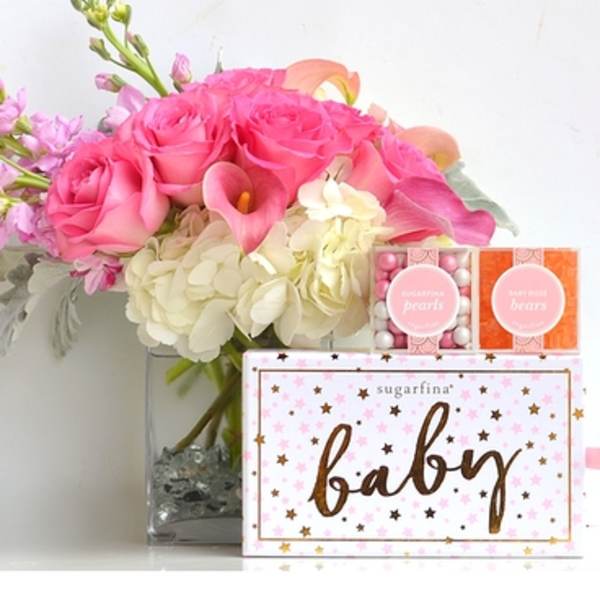 Pink roses and white hydrangeas in a glass vase with baby gift boxes