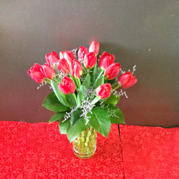 Red tulip arrangement in a yellow glass vase on a red patterned cloth
