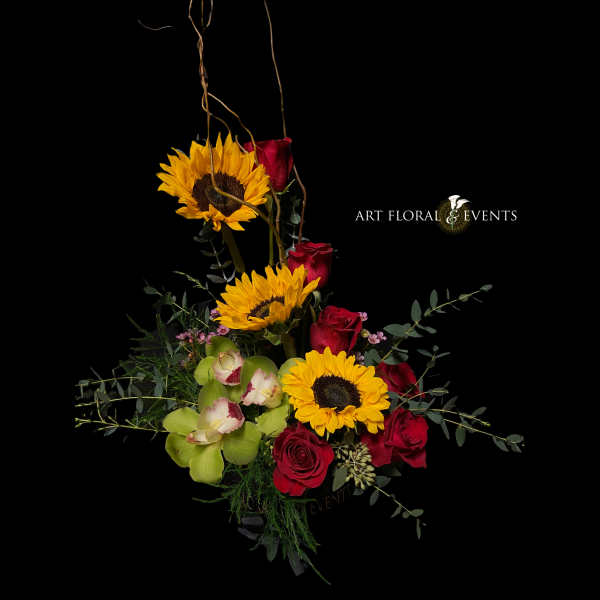 Tall floral arrangement with sunflowers, red roses, and green orchids on a black background