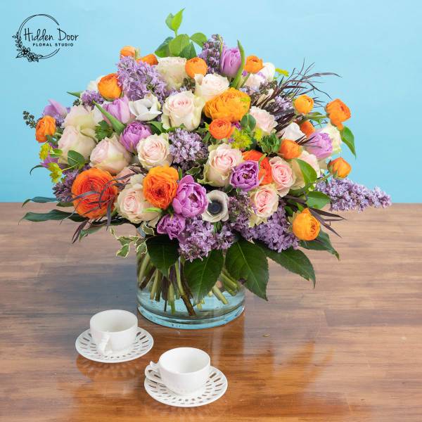 Mixed bouquet of orange, pink, purple, and white flowers in a glass vase